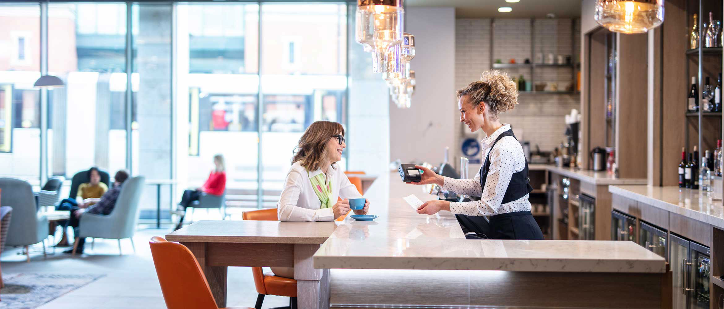 Woman working in restaurant bar giving receipt to female customer wearing glasses and white shirt