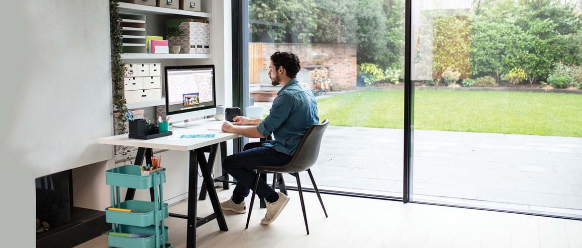 Man sat at desk looking at computer screen with shelves behind and a view of the garden through the patio doors