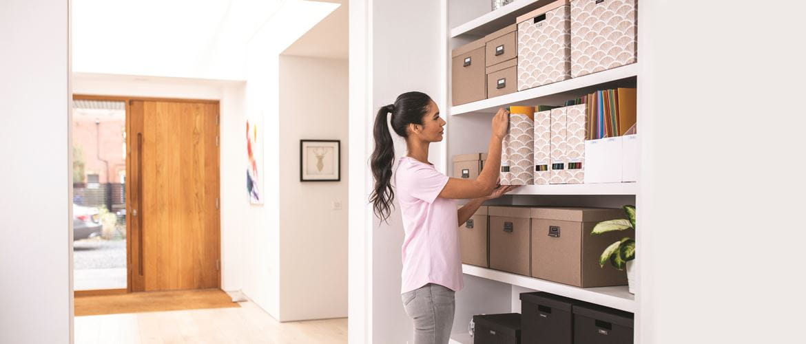 Woman stood in her home with door in the background, organising files and boxes on shelving