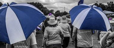 Image en noir et blanc, mais avec des touches de bleu, cette scène montre une marche caritative du Relais pour la vie sur une piste de course, alors que des dizaines de personnes aident à collecter des fonds pour une œuvre de charité. 