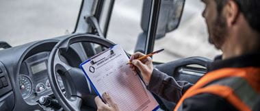 Een chauffeur in de transport- en logistieke sector bekijkt in de cabine van zijn bestelwagen een afgedrukte checklist. 