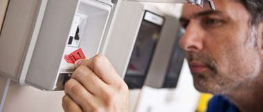 Een elektricien brengt een gedrukt etiket aan op een zekeringkast van een stopcontactpaneel. De veiligheidsingenieur plakt het etiket op om een veilige elektrische werkplek te garanderen. 