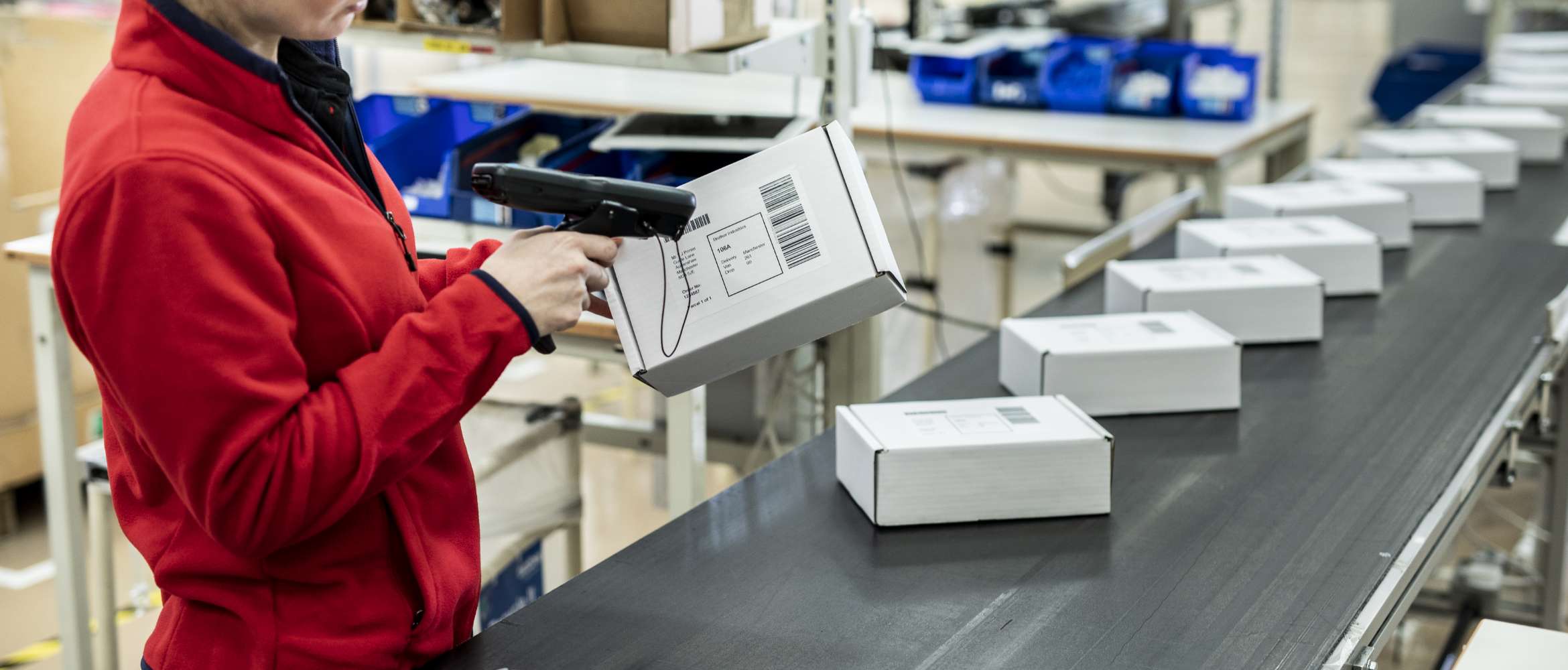 La ligne de production d'un convoyeur d'usine est remplie de colis emballés tandis qu'un ouvrier scanne une étiquette d'adresse à code-barres imprimée dans cette scène d'entrepôt de transport et de logistique.
