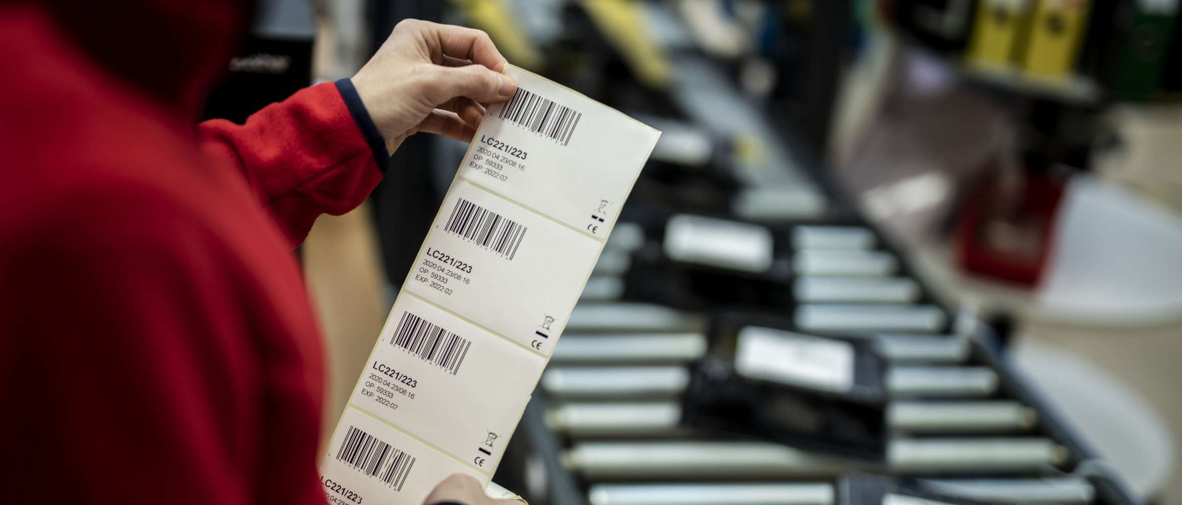 Een arbeider aan een productielijn in een productie- en logistiek bedrijf inspecteert een geprint barcode-etiket voordat het op een pakket wordt aangebracht. 