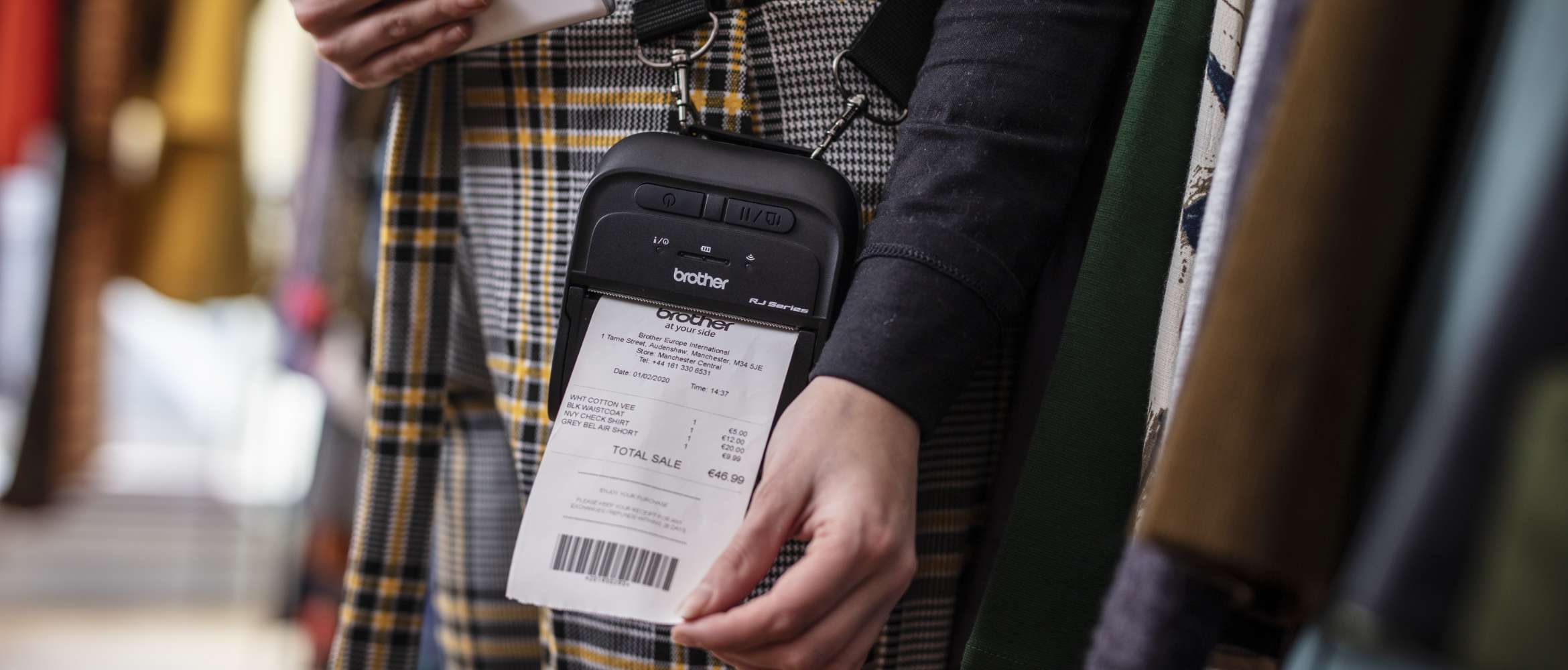 Une imprimante portable d'étiquettes et de reçus Brother est portée sur le corps d'une vendeuse d'un magasin de vêtements. Elle imprime le reçu d'un client.