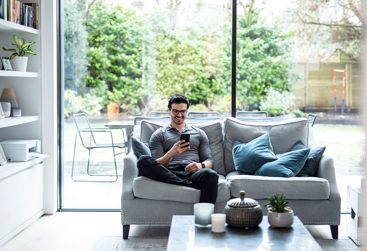 Man die zijn mobiele telefoon gebruikt zittend op zijn sofa