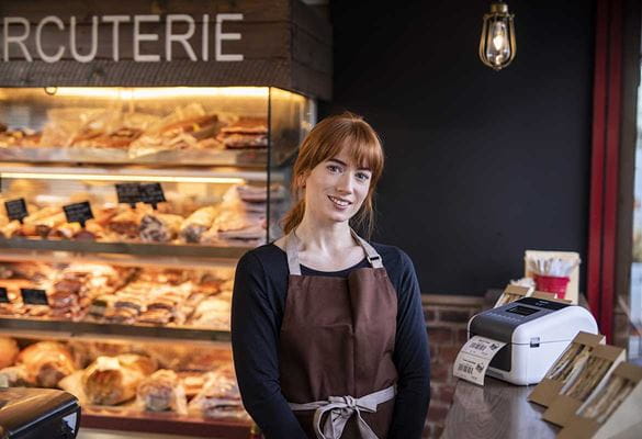 Woman wearing brown apron in cafe with sandwiches and TD label printer