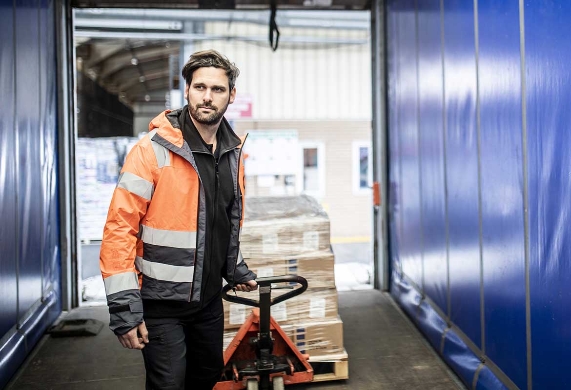 Man wearing orange hi-vis coat pulling pump truck with boxes in truck with blue sides