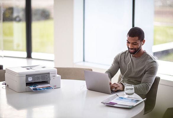 Un homme travaillant assis à côté d'une imprimante Brother wifi