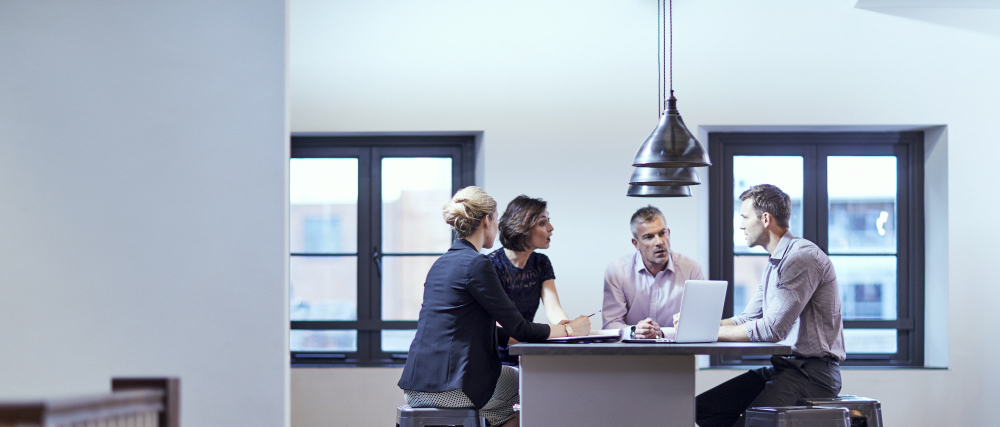 A group of males and females sat at a desk talking