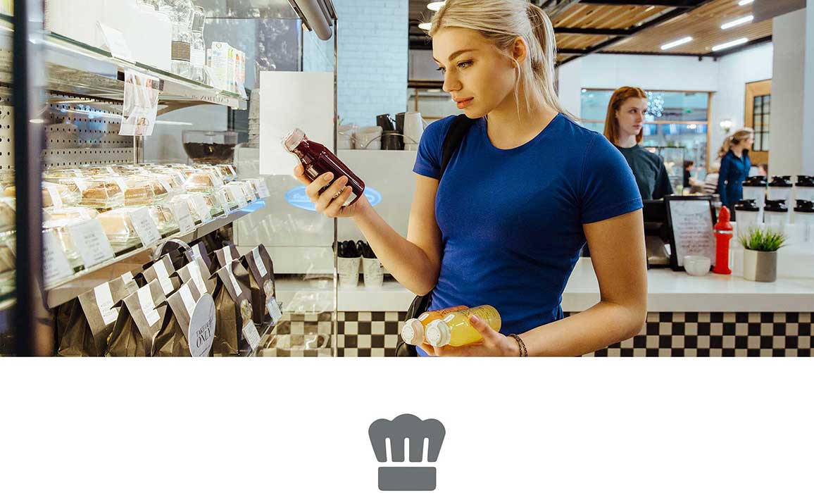 Woman with blond hair wearing blue tshirt looking at a juice bottle holding sandwich