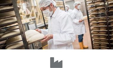 Men working at an industrial bakery and about to put bread in the oven