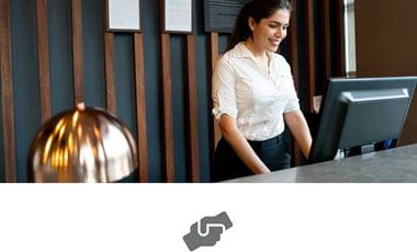 Female receptionist with dark hair tied back wearing white shirt holding at reception using computer