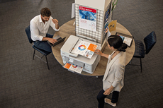 Luchtfoto van een man en een vrouw in een kantoor, kleurendocumenten op de printer, tafel, stoelen