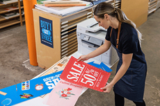 Vrouw houdt afgedrukte lang formaat banner vast, printer, schappen