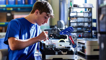 Man in blauwe T-shirt met gereedschap die aan een printer op een werkbank werkt