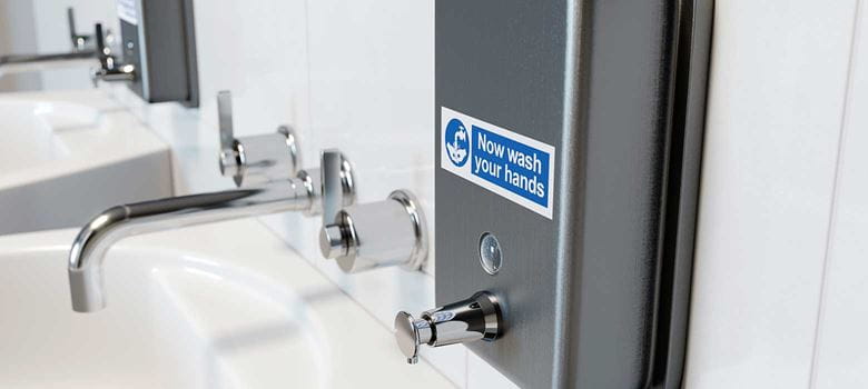 Label aangebracht op een zeepdispenser boven een wastafel dat vraagt om de handen te wassen