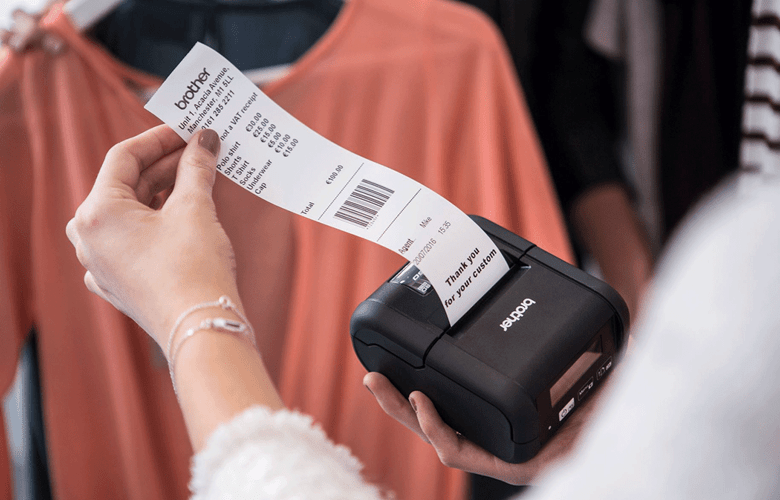 Vrouwelijke winkelbediende in klerenwinkel overhandigt ontvangstbewijs afgedrukt met RJ printer