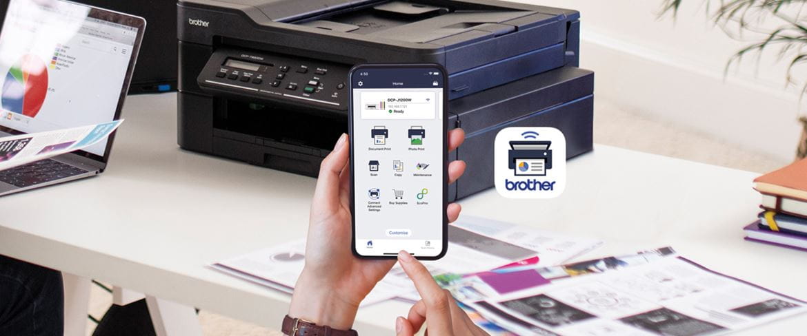 O aplicație de imprimare mobilă Brother pe un telefon, văzută pe fundalul unei imprimante Brother negre pe un birou.