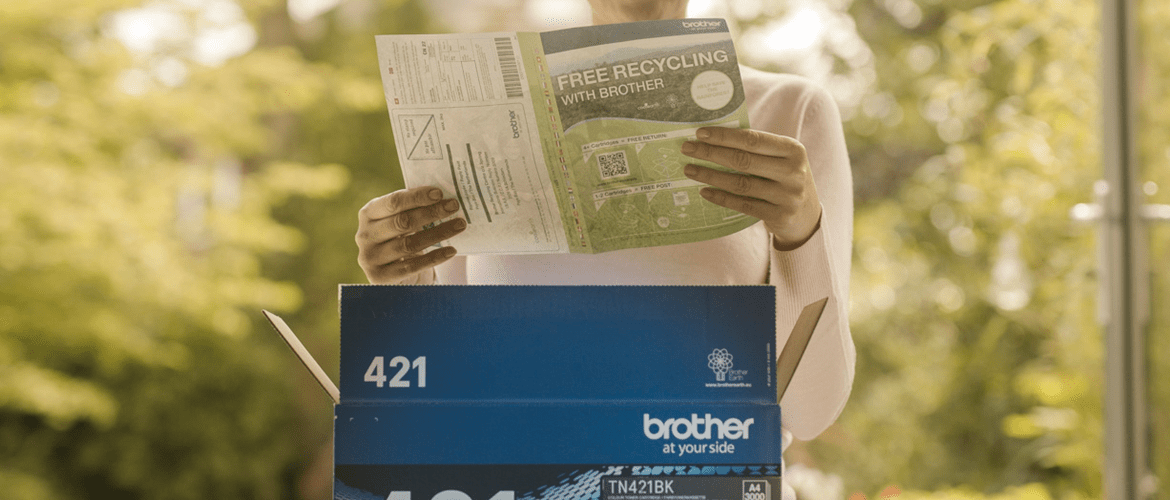 A woman reading recycling instructions on a green paper behind a blue, Brother toner cartridge box