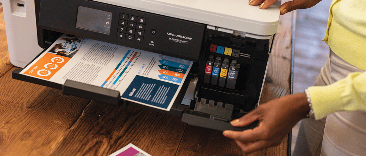 O femeie ne arăta cele 4 consumabile CMYK ale imprimantei care are in tava un print color.
