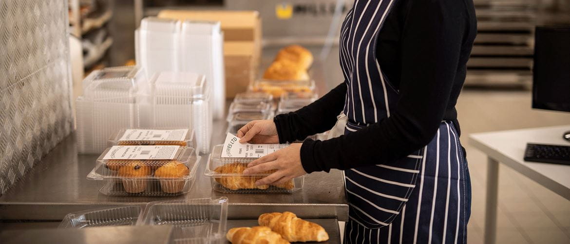 Az alkalmazott csomagolt croissant-t és muffint címkéz a konyhában