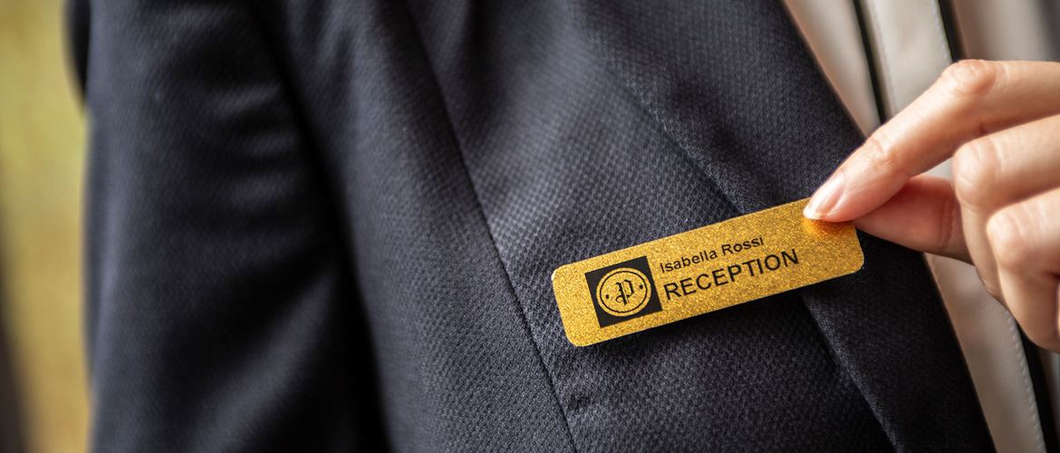 Hotelový recepční má na sobě štítek se jmenovkou s černým tiskem na zlatém podkladu