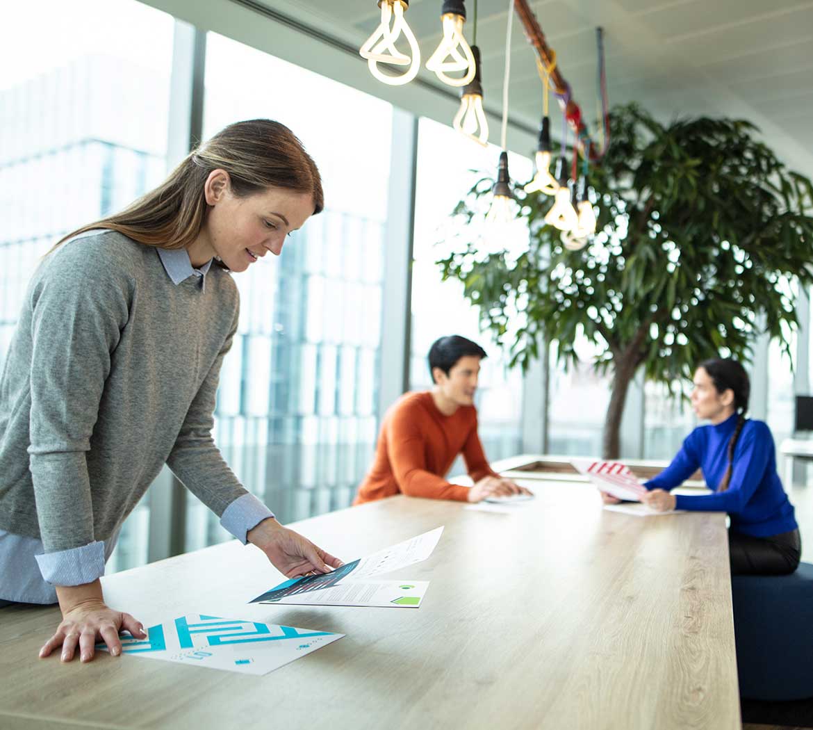 A long desk with a woman looking at documents and two people sat talking