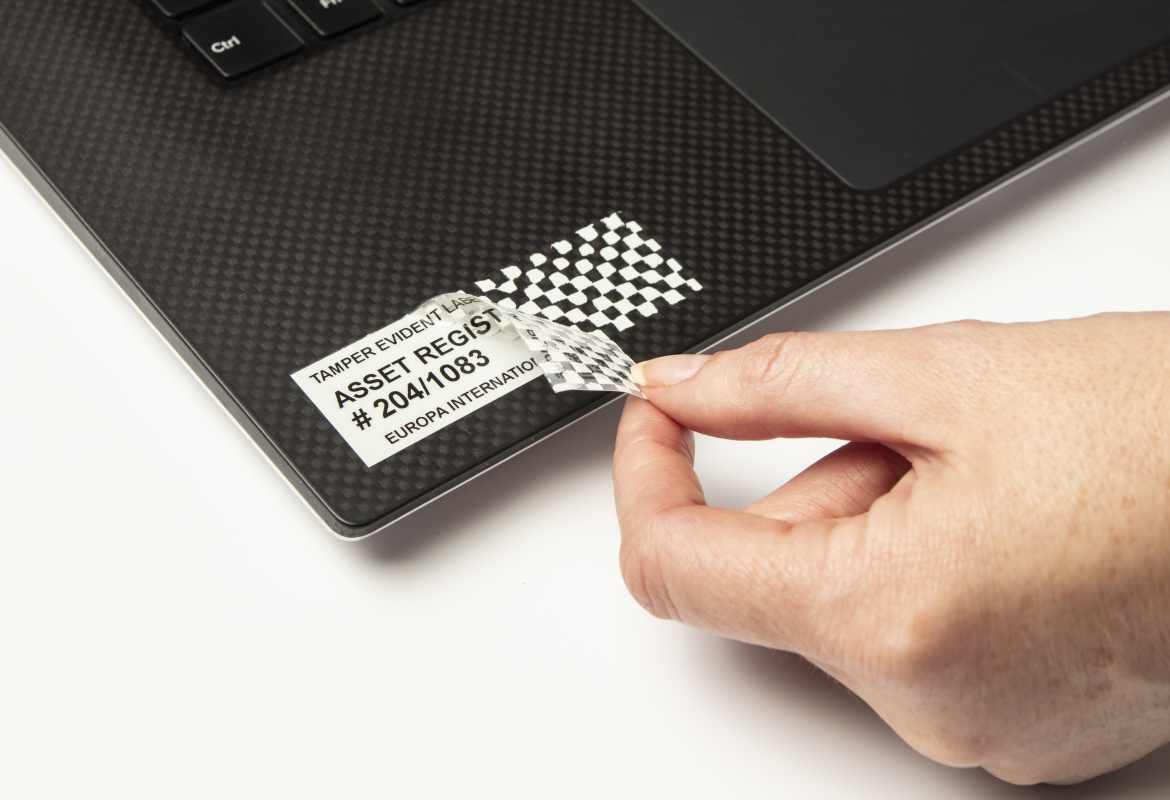 Persoană care scoate o bandă de securitate de pe un laptop, iar eticheta lasă o amprentă hașurată