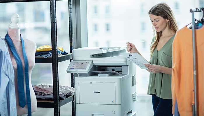 Nő, aki dokumentumot tart a többfunkciós nyomtatónál, ruhák között és próbababa közelében