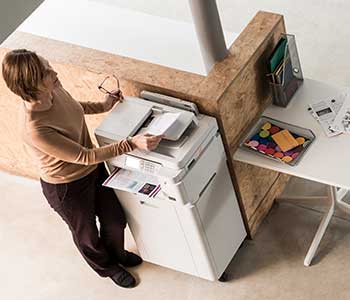 Žena u bež majici stoji pored pisača i skenira dokumenta, stol, dokumenti