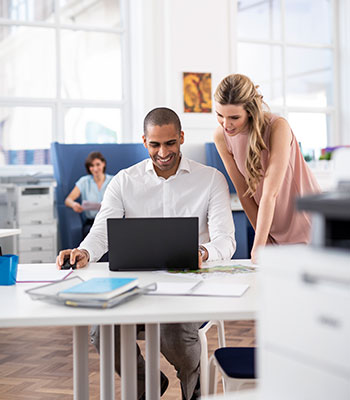 Жена с очила стои с чаша в ръка, мъж стои на бюро в зает офис, принтери, мъж в костюм, компютри