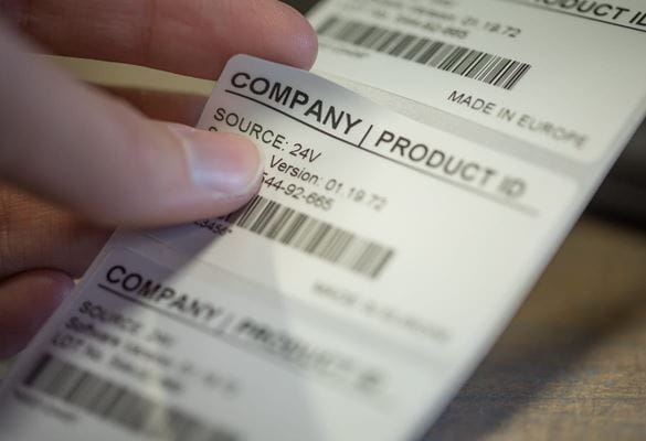 Detailní záběr na osobu, která odlupuje samolepicí štítek ID na míru s identifikací výrobku společnosti z rolky štítků