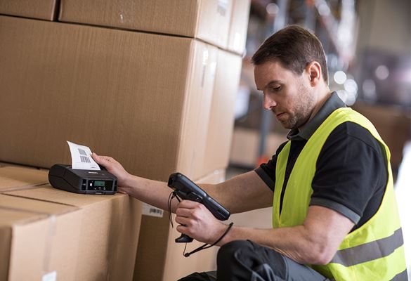  Čovjek koji nosi hi-vis drži naljepnicu sa skenerom, štampač etiketa na vrhu kutija u skladištu