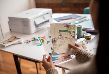 Femeie ținând mai multe cărți colorate cu o imprimantă și role de sfoară pe o masă în fundal