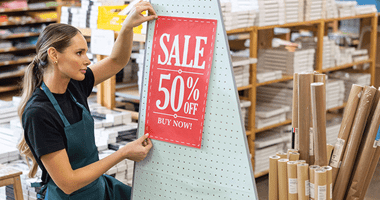 Kobieta trzyma duży plakat z ceną próbując go umieścić w sklepie
