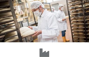 Egy ipari pékségben férfiak dolgoznak, akik kenyeret készülnek a sütőbe tenni