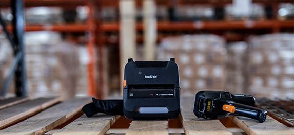 Crni mobilni RJ pisač na polici u skladištu, kutije, palete, ručni skener 