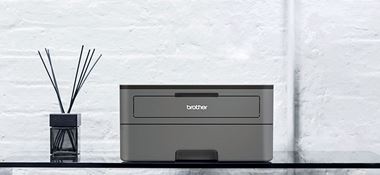 Temno siv črno-beli laserski tiskalnik HL-2350DW na stekleni mizi z osvežilcem zraka