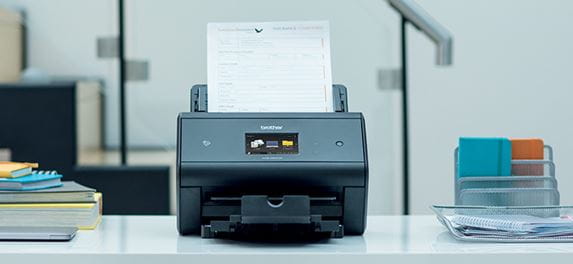 Brother ADS-3600W namizni dokumentni skener skenira na mizi poleg pisarniške opreme