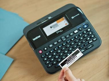 Tiskalnik nalepk Brother P-touch D600 z roko, ki drži nalepko za inventar