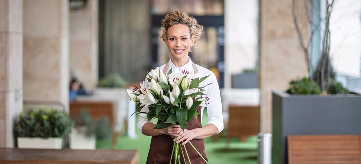 Virágüzletben az eladó  egy csokor liliomot tart, növények, asztal, szabadtéri székek