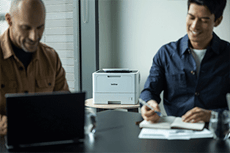 Két férfi ül az irodában az asztal körül, Brother HL-L5210DW, laptop, jegyzettömb, toll, A4-es fekete-fehér dokumentumok