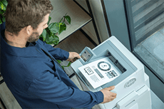 Felülnézetben a Brother HL-L6410DN nyomtató, a férfi fekete-fehér A4-es dokumentumot néz a nyomtatóban
