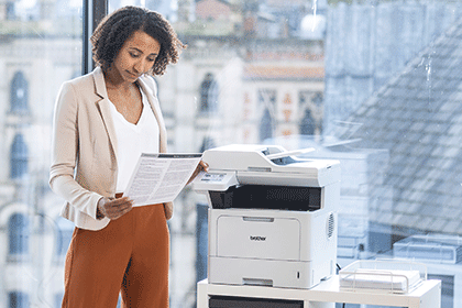 Femeie care stă lângă Brother MFC-L5710DN ținând un document mono
