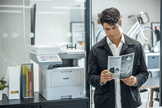 Férfi az MFC-L6910DN nyomtató mellett áll, kezében fekete-fehér dokumentumok