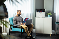 Muž držiaci plnofarebný obojstranný výtlačok, sediac vedľa tlačiarne Brother DCP-L3520CDW 