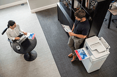 pohľad zhora na kanceláriu, žena držiaca farebný dokument, muž stojaci pri tlačiarni Brother