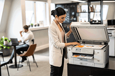 Žena v kanceláři s mužem v pozadí skenuje dokument na multifunkční tiskárně