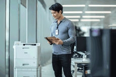 Mężczyzna w biurze trzymający ipada stoi obok drukarki